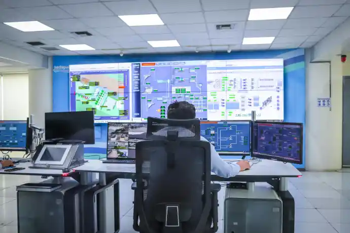 Engineer working on multi-screen industrial control room with plant design models